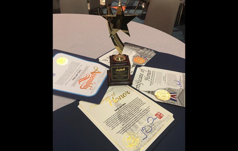 A statuette and four certificates are presented on a table. The statuette depicts a star suspended in the air with a comet-like tail. The certificates are stylishly placed flat on the table, fanning around the statuette.