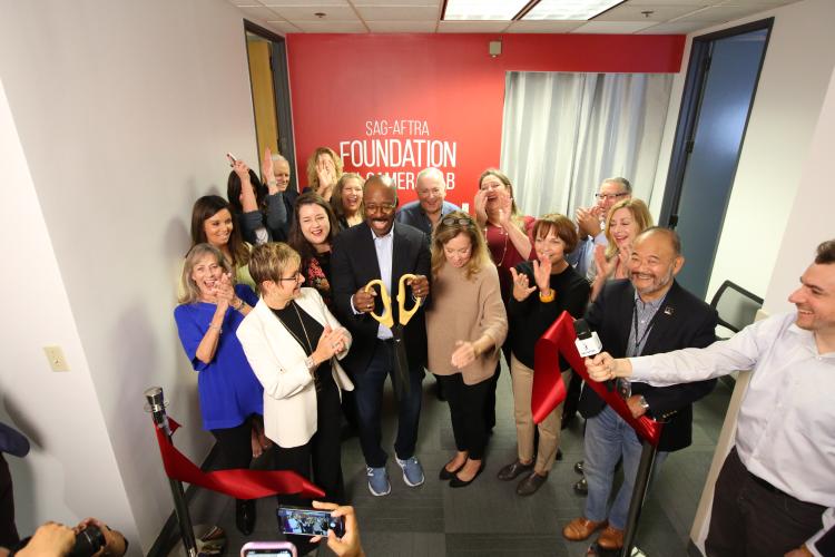 Action Shot of Vance cutting red ribbon with members all around him. 