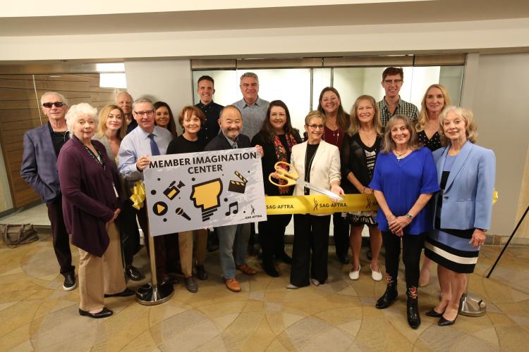 Large group photo holding Imagination Center poster board, Carteris holding large scirros behind a yellow "SAG-AFTRA" ribbon.