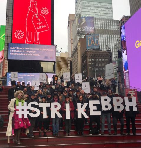 Members stand on the steps in Time Square holding #StrikeBBH letters