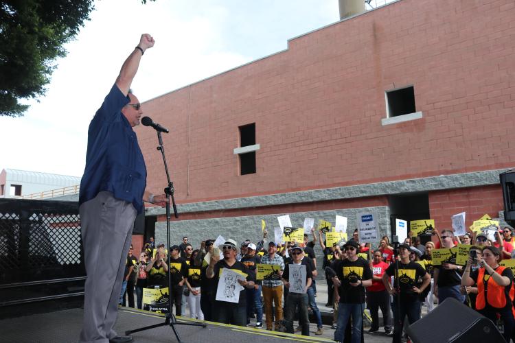 Herrera standing at microphone holding right fist in the air looking out at the crowd