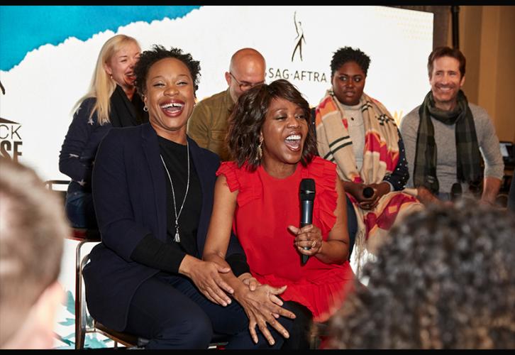 Two seated African-American women, one in blue the other in red, laugh together.