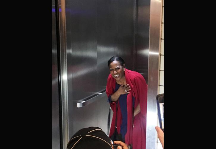 Vickie Thomas, en el medio del plano, está dentro del ascensor. En primer plano hay un fotógrafo y otras personas sosteniendo teléfonos con cámara.