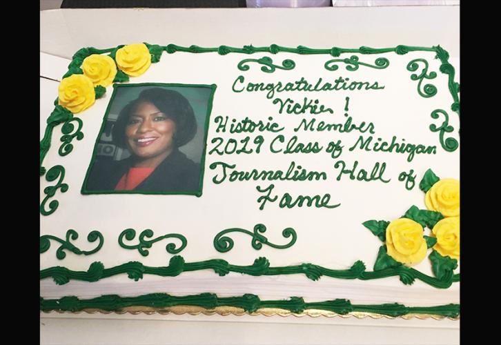 Una imagen de un pastel con la foto de Vickie Thomas en la cabeza y las palabras "¡Felicitaciones Vickie! Miembro histórico de la promoción 2019 del Salón de la Fama del Periodismo de Michigan" en glaseado verde.