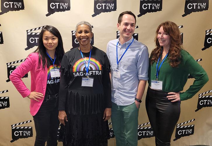 Three women and a man wearing lanyards pose for a photo in front of the CT Film & TV backdrop. 