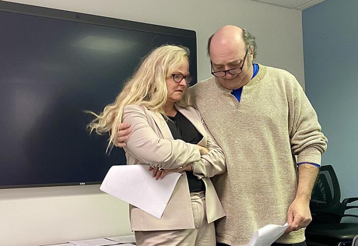 Siriani puts his arm around Zella and looks down. Both hold scripts.