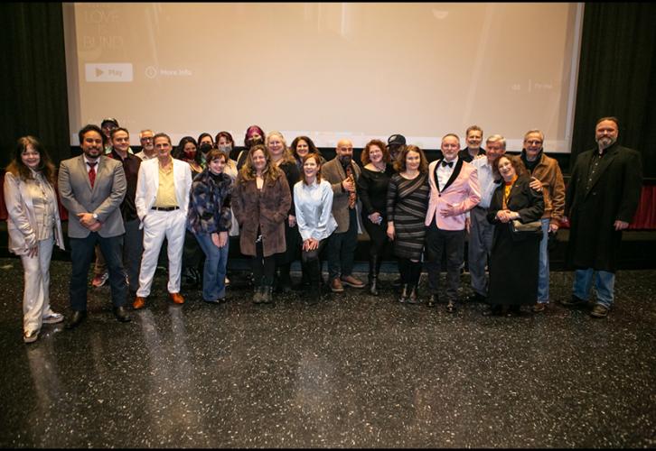 A group photo of a large crowd in a theater-like setting. Behind them is a large projection screen.
