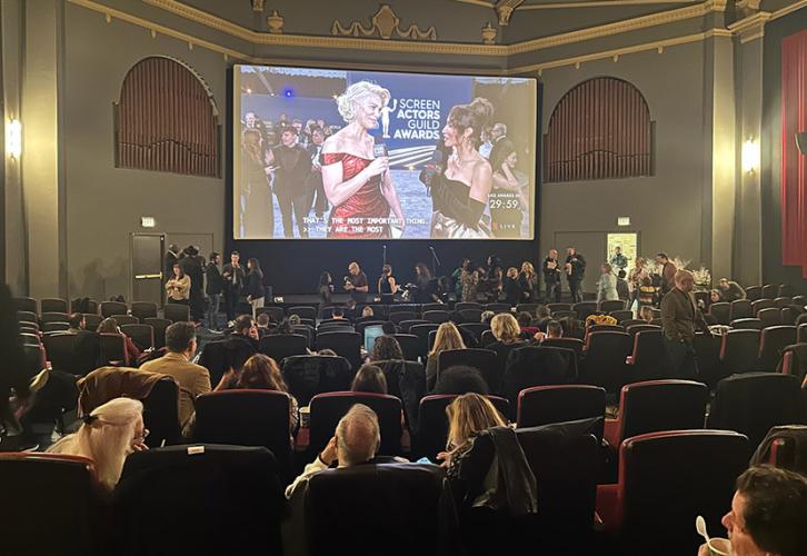 Members and their guests sit in a theater watching a large screen streaming the SAG Awards.