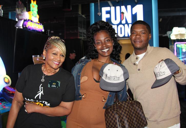A woman in a black shirt, a woman in a brown dress and a man in a cream-colored sweater pose with vintage SAG Award hats. 