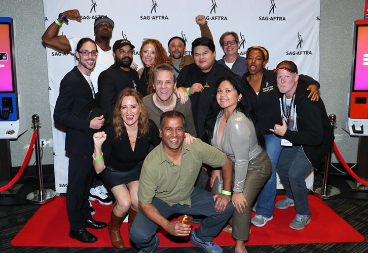a group of men and women pose on a red carpet with a SAG-AFTRA backdrop behind them.