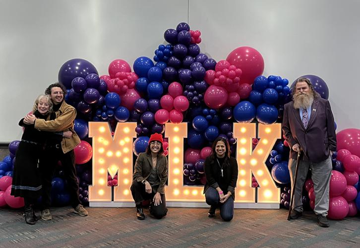 Crawford, Bellardinelli, Cabanela, Gupta and Scullin stand in front large illuminated letters "MLK" as well as blue and red balloons.