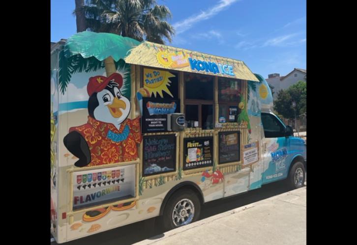 A shave ice truck is parked at the curb.