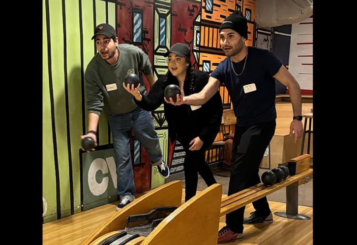 Three members stand side-by-side in the lane posing with bowling balls as if throwing them.