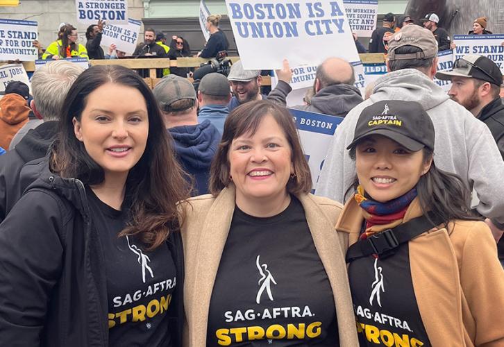 Carrol, Maher and Eng smile for the camera at a labor rally. All three wear SAG-AFTRA Strong shirts and signs are visible in the background reading "Boston is a union city."