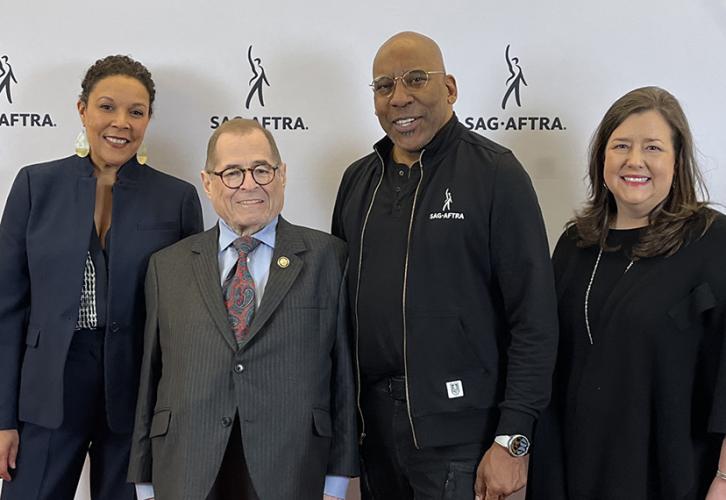 A diverse group of people stand in front of a white backdrop with Sag-Aftra written in black.