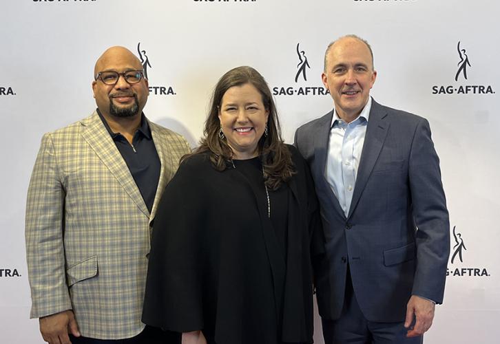 Three people smile in front of a white step-and-repeat with Sag-Aftra in black text.