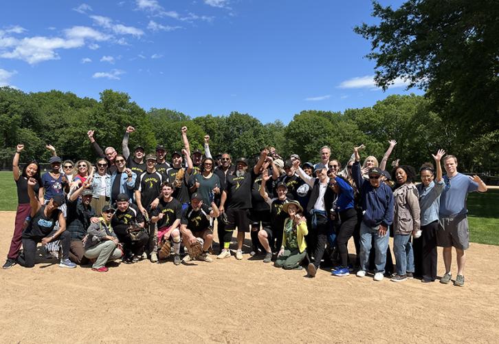 A diverse group of people pose on a baseball field.