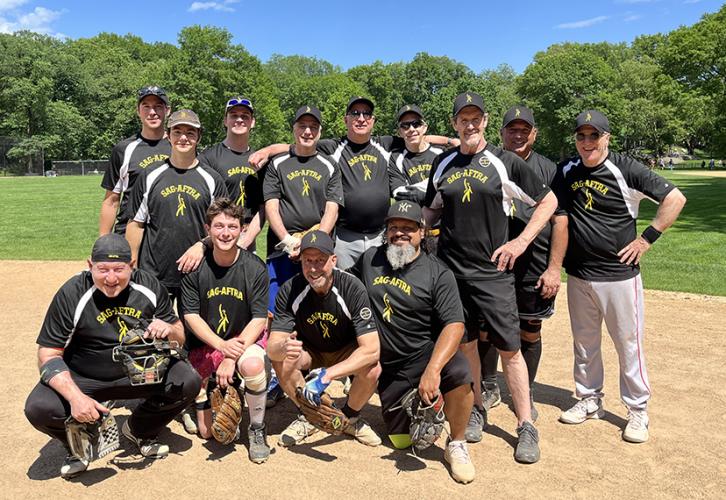 A group of men in black and yellow jerseys and black baseball caps that say Sag-Aftra gather on a baseball field.