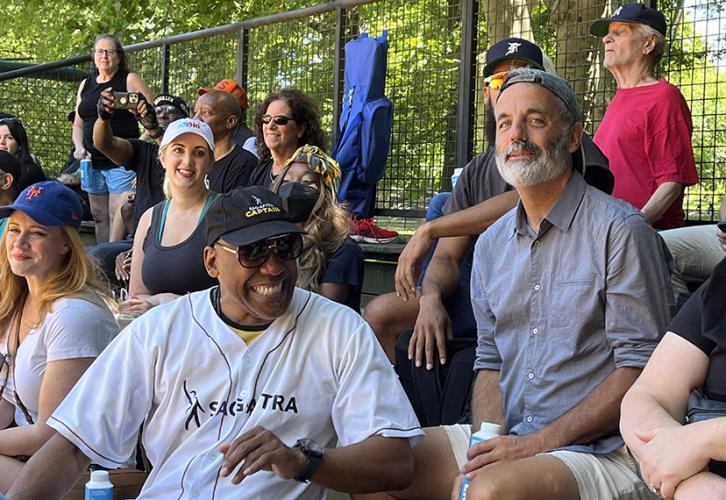 Knight wears a black baseball cap and white jersey with a black SAG-AFTRA logo. He sits in the bleachers with other SAG-AFTRA members.