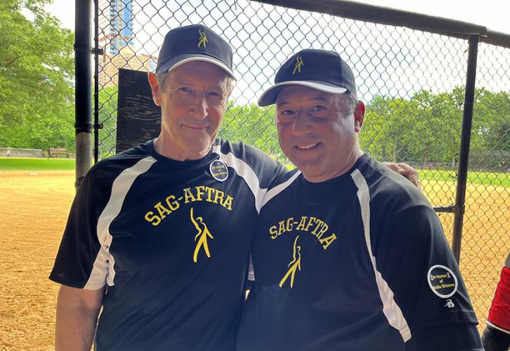 Two men wear black baseball caps and black jerseys with SAG-AFTRA written in yellow text across the chest. Both men wear patches that read “In Memory of leslie Shreve.”
