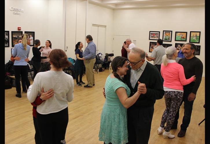 Un grupo diverso de hombres y mujeres, en parejas, realizan movimientos de pantomima de baile de salón.