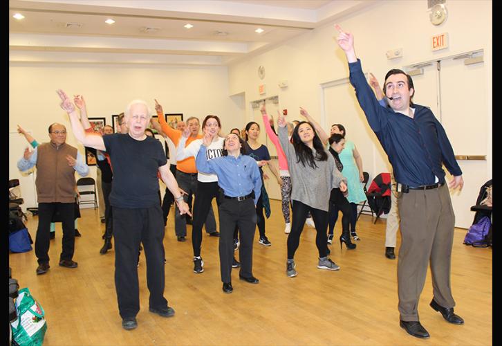 Un caballero a la derecha pantomina un movimiento de baile. Detrás de él, un grupo diverso de hombres y mujeres, sigue sus movimientos.