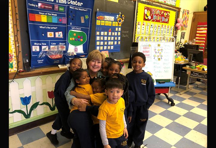 A woman is hugged by small, smiling African-American children wearing blue and yellow uniforms.