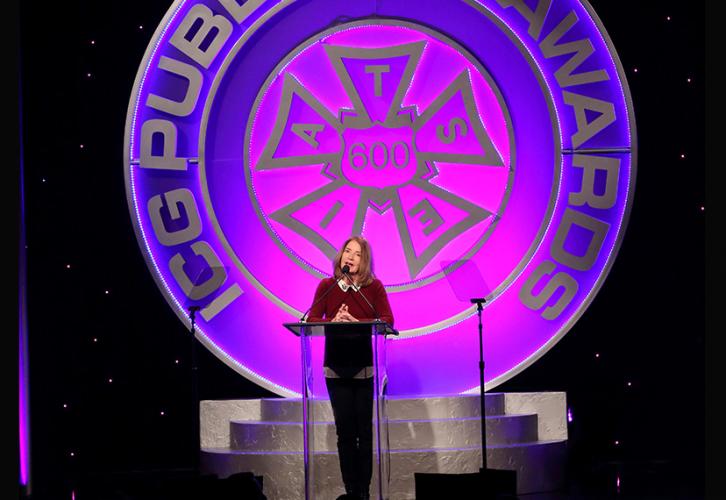 Screen Actors Guild Executive Producer Kathy Connell stands at a podium onstage with the IATSE symbol behind her. 