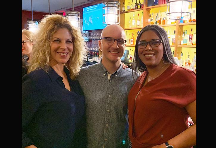 Two women and one male smile directly at the camera in a restaurant/lounge area. 