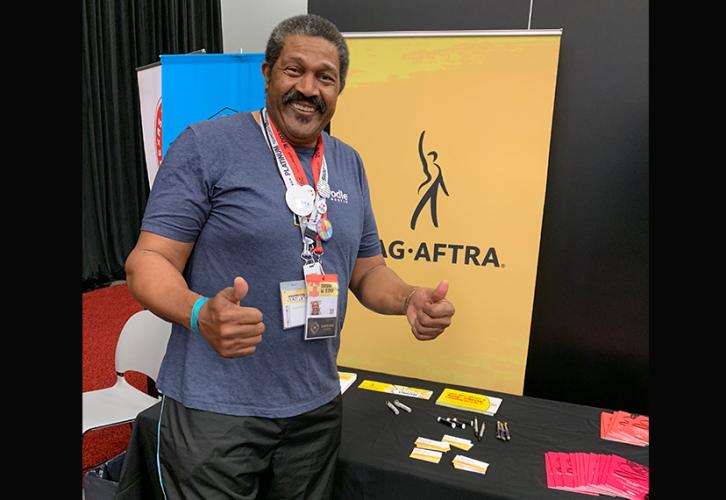 An African-American gentleman stands at a table with information about SAG-AFTRA and the union banner. 