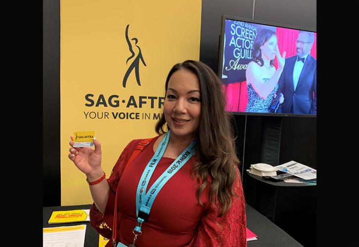 A woman in a red dress and SXSW name tag holds up her membership card. 