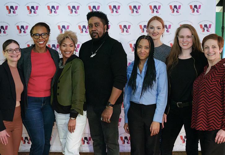 The group smiles for the camera in front of a backdrop with the Women in the Arts & Media Coalition logo.