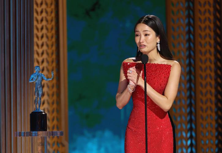 Anna Sawai is on stage. She turns to her right and clasps her hands in front of her. Beside her is the SAG Awards statuette. 