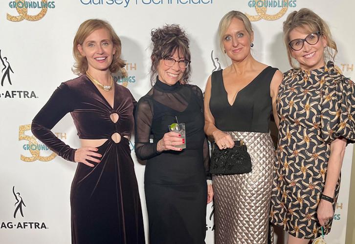 Four women in dresses stand on the red carpet. Each is wearing a cocktail dress. Behind them is a white step-and-repeat backdrop with The Groundlings 50th Anniversary, SAG-AFTRA and Gursey-Schneider logos.