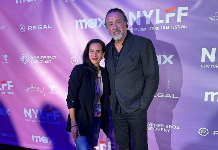 Morales and Rodriguez stand in front of a blue step-and-repeat backdrop with various logs in white text. Both are dressed in business casual attire. The lighting is a cool blue.
