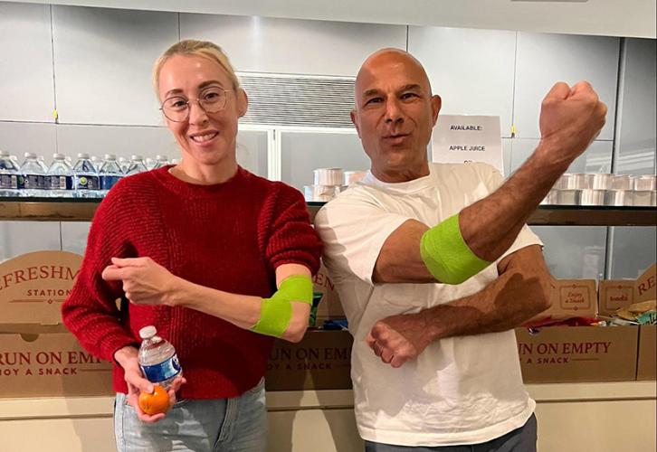 Two individuals show off their arms with neon green wraps on them. One holds a clementine and small water bottle.