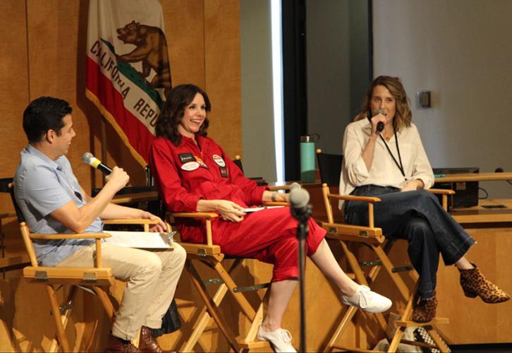 Three individuals sit talking in directors chairs with wood paneling behind them and a California flag.