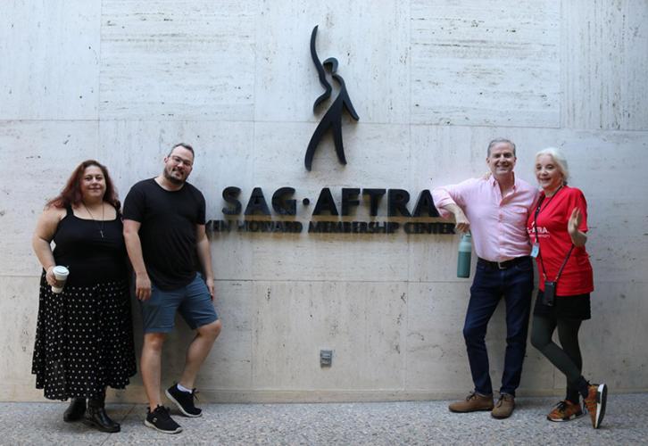 Four individuals pose around the SAG-AFTRA logo that is mounted on a building.