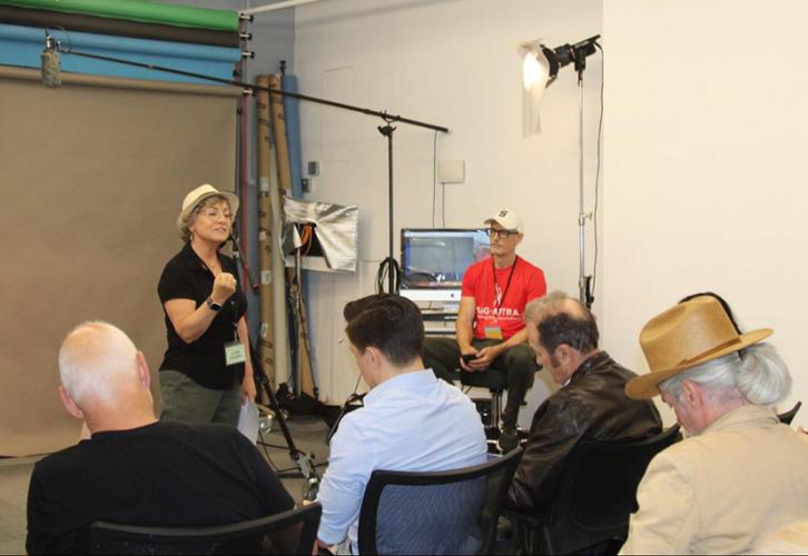 A person with a backdrop behind them teaches a group of people in a classroom.