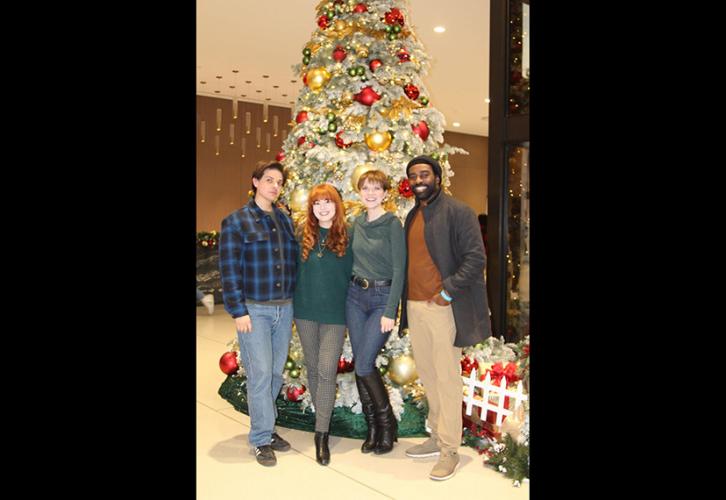 Four individuals pose in front of a decorated Christmas tree.