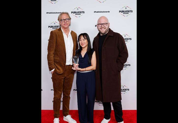 De izquierda a derecha, Brockett, Nguyen y Vivas están en la alfombra roja. Nguyen lleva un vestido azul y sostiene su estatuilla; Vivas lleva un abrigo marrón sobre un conjunto completamente negro. Detrás de ellos, un telón blanco con el logo de los premios.