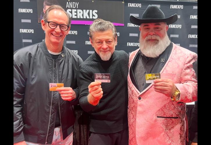 Three individuals take a photo in an exhibition hall. Serkis wears a black turtleneck and gray slacks. Each of them holds a SAG-AFTRA membership card. Behind them is a black Fan Expo New Orleans step-and-repeat backdrop.