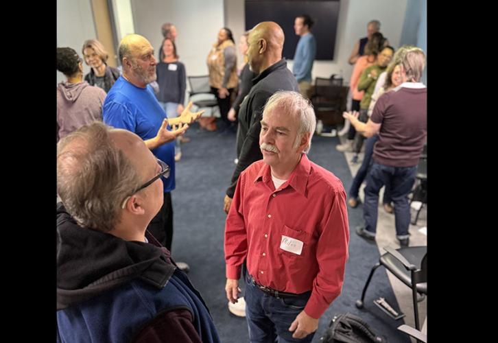 SAG-AFTRA members pair up around the conference room to participate in an acting exercise; one pair – a person in a red button-down and a person in a black and blue hoodie – can be seen in the foreground.