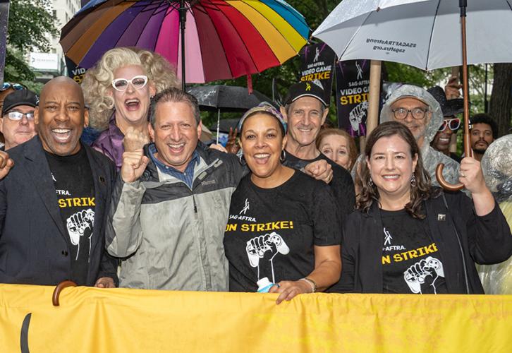 A group of people stand behind the SAG-AFTRA parade banner with black text on a yellow background.