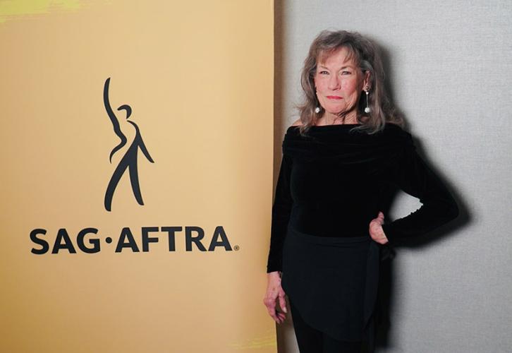 A person dressed in all black smiles next to a SAG-AFTRA banner.