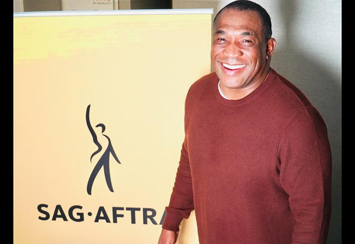 A person in a maroon sweater smiles next to a SAG-AFTRA banner.