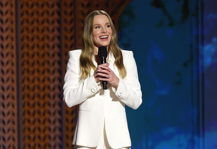 Kristen Bell stands on stage. She holds a microphone.