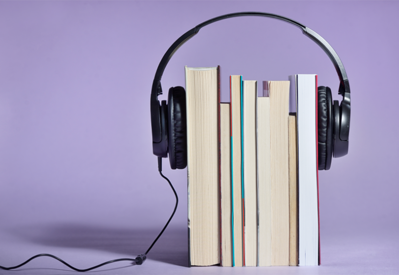 Audiolibros de SAG-AFTRA Una pila de libros se mantiene unida mediante unos auriculares de audio sobre un fondo violeta.