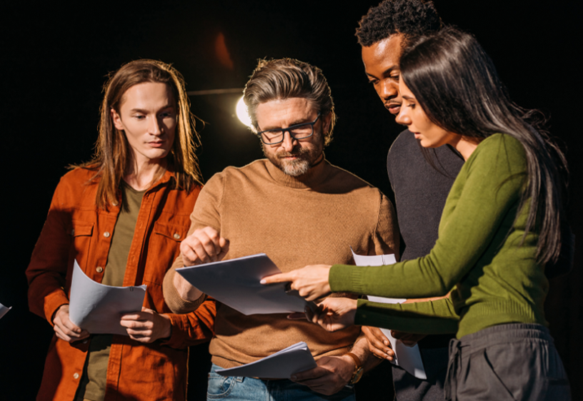 New England Local Conservatory Four diverse individuals are looking over a script. A light shines behind them.
