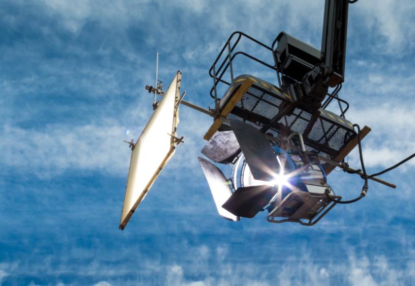 A hanging HMI daylight projector on a crane against a blue sky with clouds